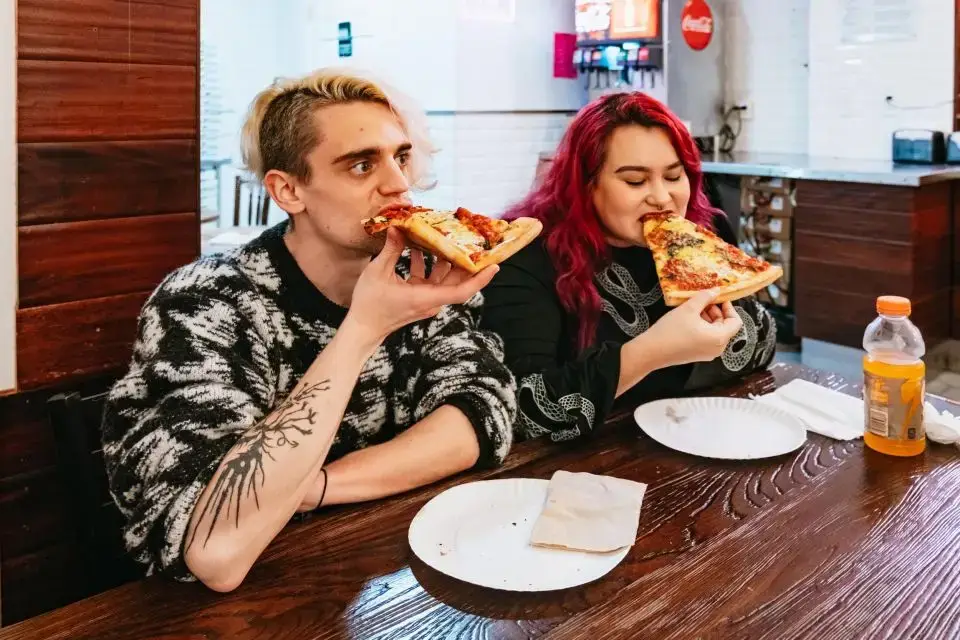 a woman eating a slice of pizza sitting on top of a wooden table
