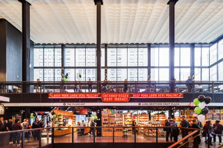 an airy indoor food market with people ordering food at stands