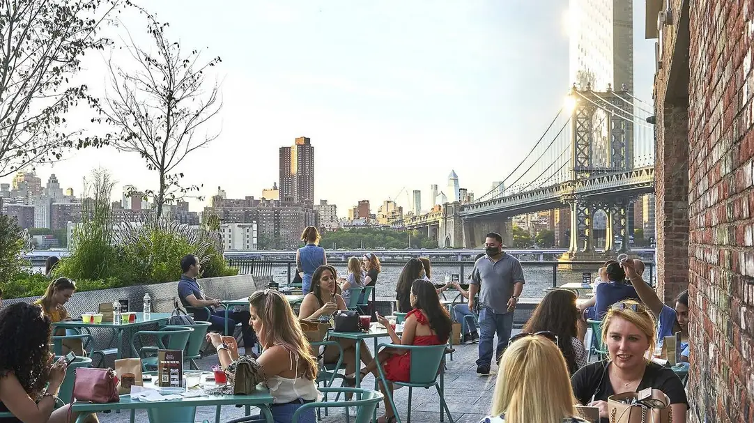 NYC's Best Markets: Food Markets, Flea Markets & More! | Like A Local Tours people sitting outside at tables and eating with the manhattan bridge in the view