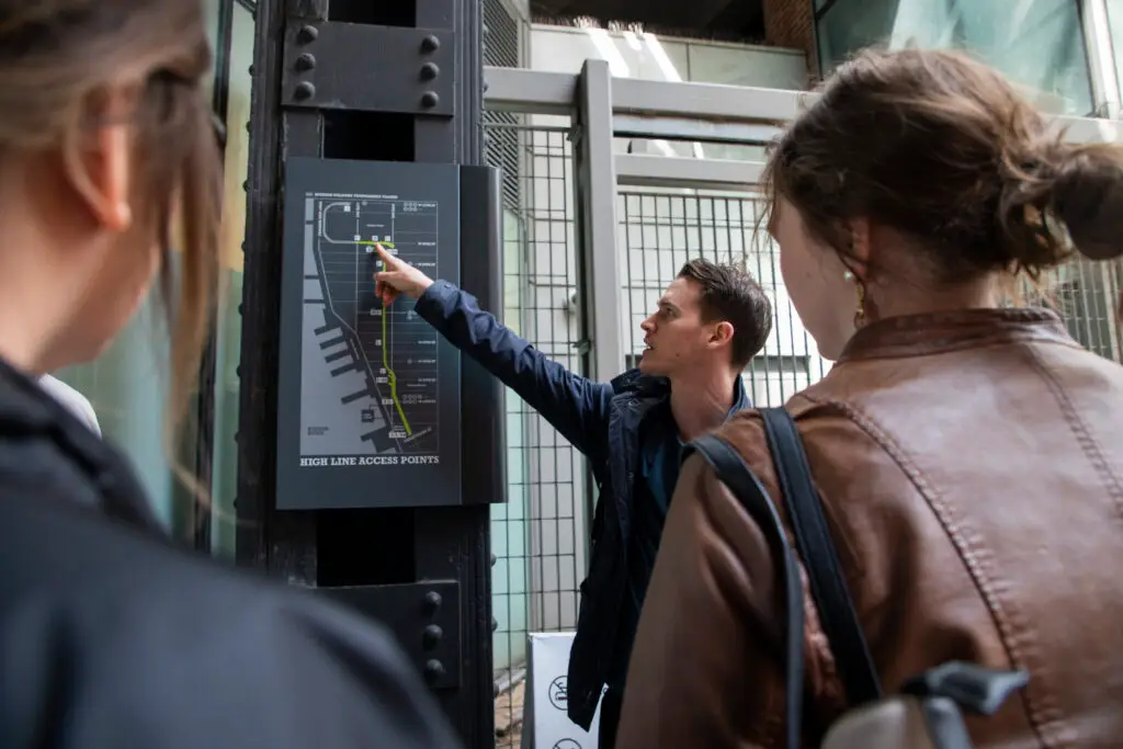 Tour guide pointing to a High Line map sign as two guests look on