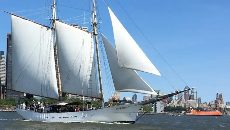 Tall ship with white sails on the Hudson River, with the Manhattan skyline behind it