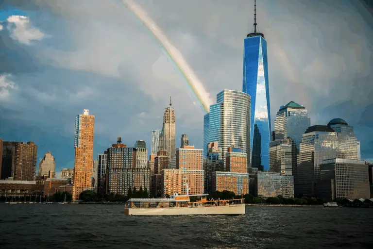 Sightseeing yacht on the Hudson River below the Lower Manhattan skyline, with a rainbow over One World Trade Center