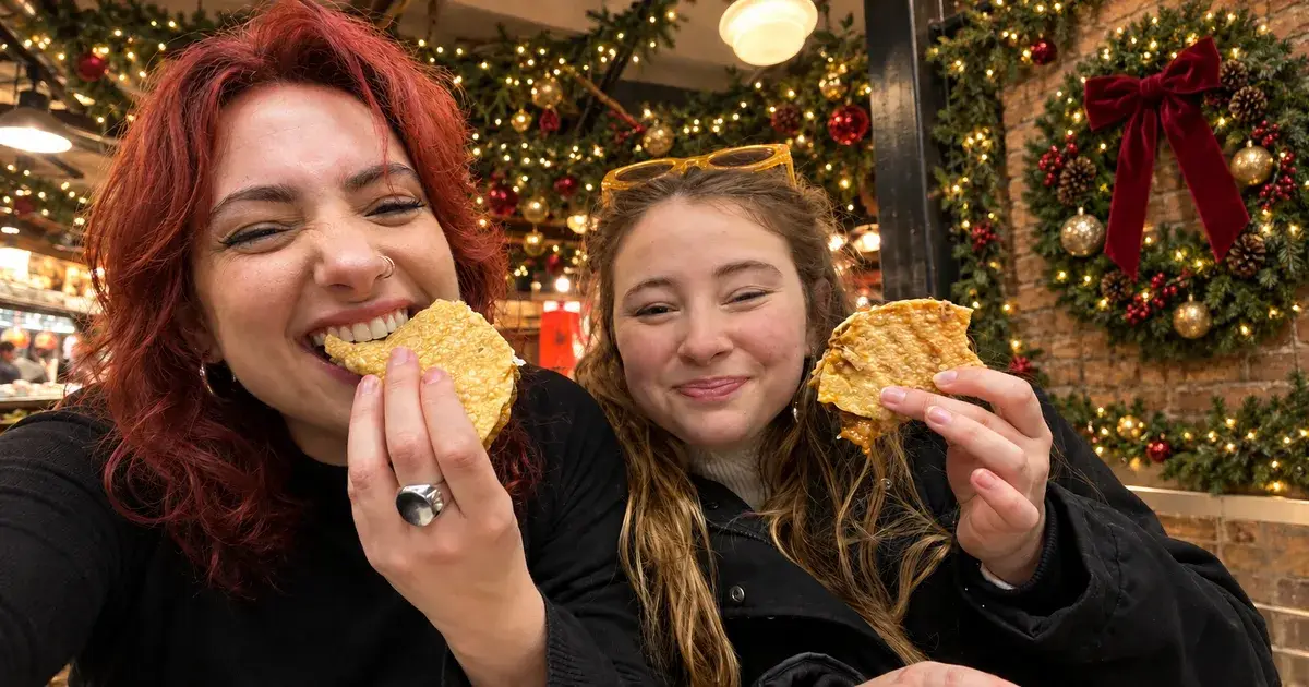 Two guests laughing and eating crispy treats under holiday garlands and a red-bow wreath at Chelsea Market