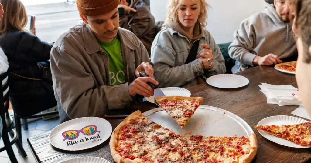 Guests sharing a whole NYC pizza with a Like A Local Tours plate on the table