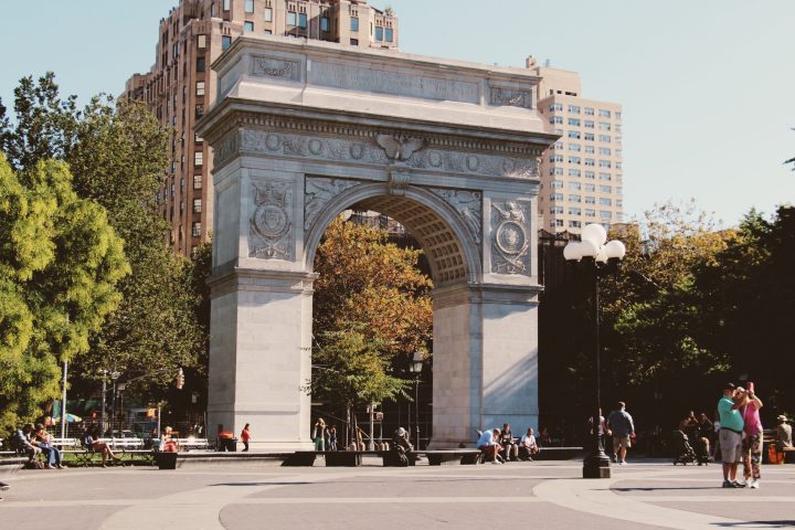 a group of people walking in front of a statue with Washington Square Park in the background